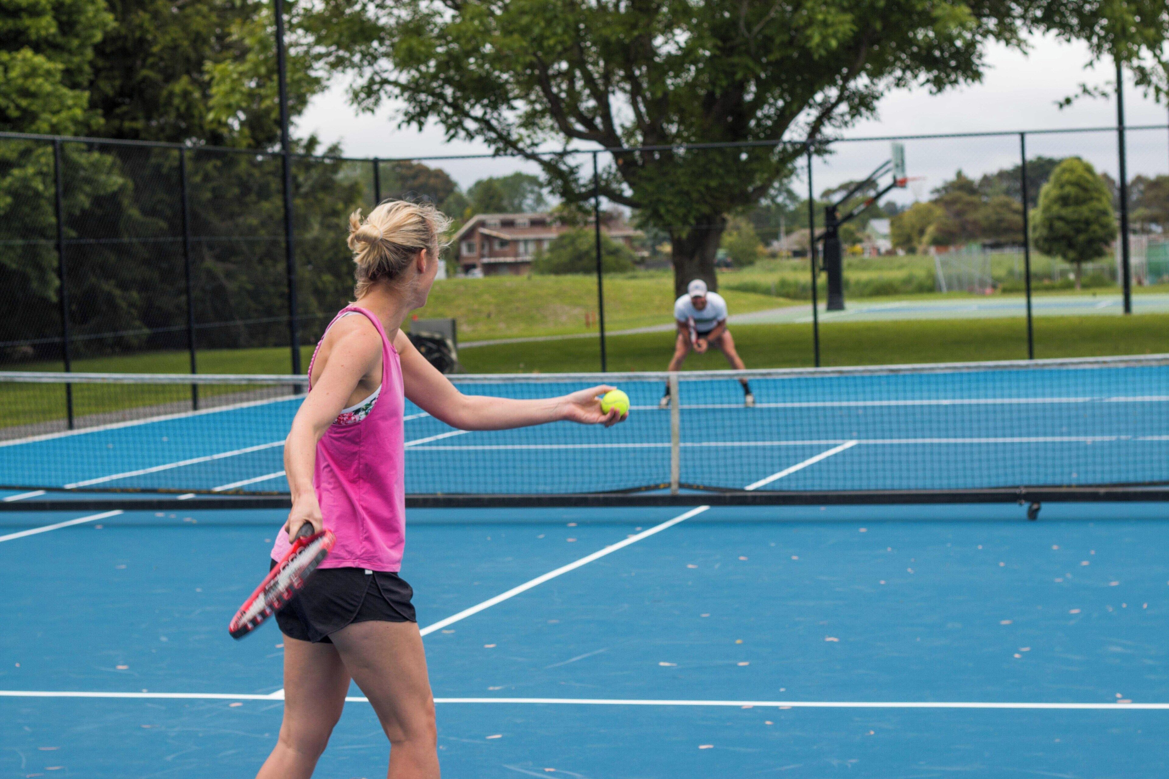 A tennis court with a net, a player in a pink top and black shorts, and another player in the background.