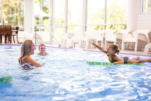 Una piscina interior con agua cristalina, una silla de salvavidas y una zona junto a la piscina con sillas y una mesa.