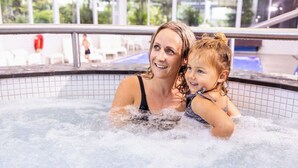 A woman and a child in a hot tub with a glass roof and outdoor seating area in the background. - Commodore Airport Hotel (Christchurch)