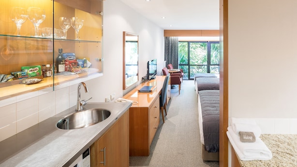 A modern kitchen with a stainless steel sink, a dining area with a table and chairs, and a view of the garden through large windows. - Commodore Airport Hotel (Christchurch)