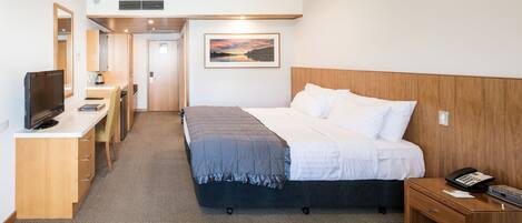 A hotel room with a bed, bedside table, TV, desk, and a painting on the wall.