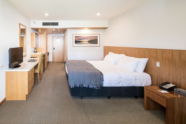 A hotel room with a bed, bedside table, TV, desk, and a painting on the wall. - Commodore Airport Hotel (Christchurch)