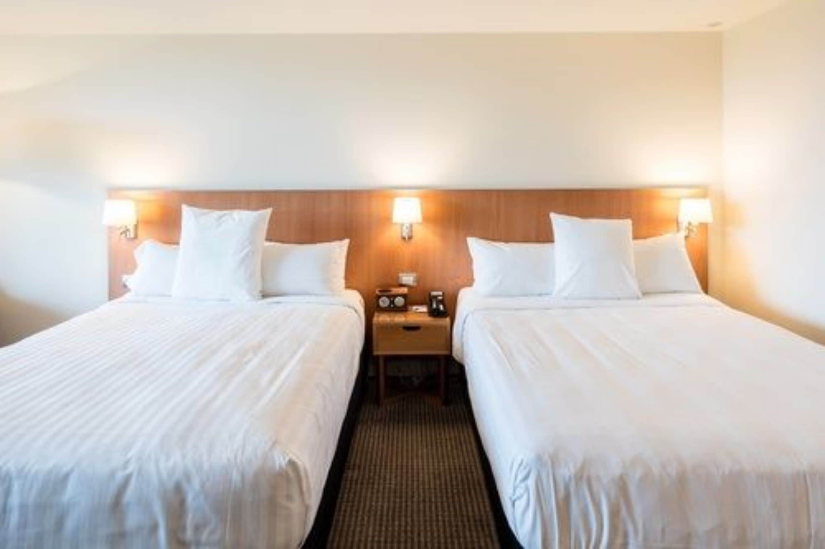 A hotel room with two single beds, a wooden headboard, bedside lamps, a nightstand with a radio, and a carpeted floor.