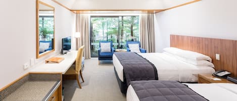 A hotel room with two beds, a desk, a chair, a TV, and a view of the outdoors.