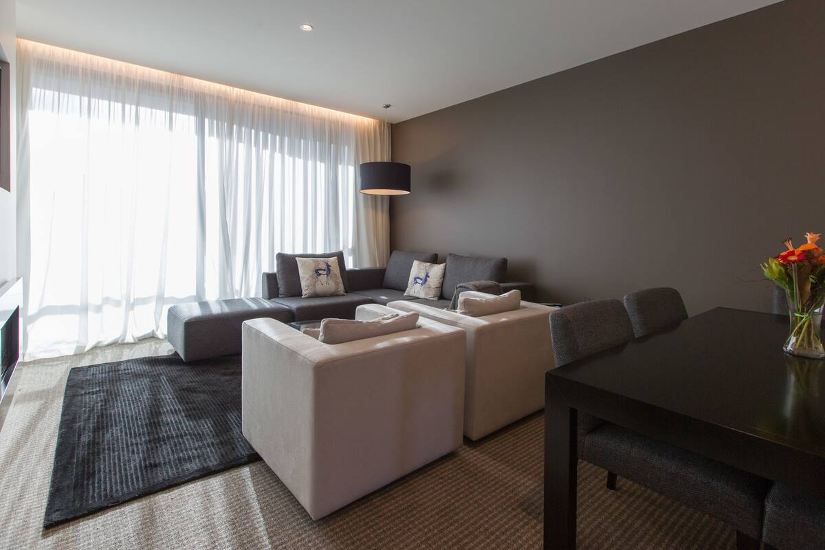 A modern living room with a grey sofa set, a dining table, and a vase with flowers.