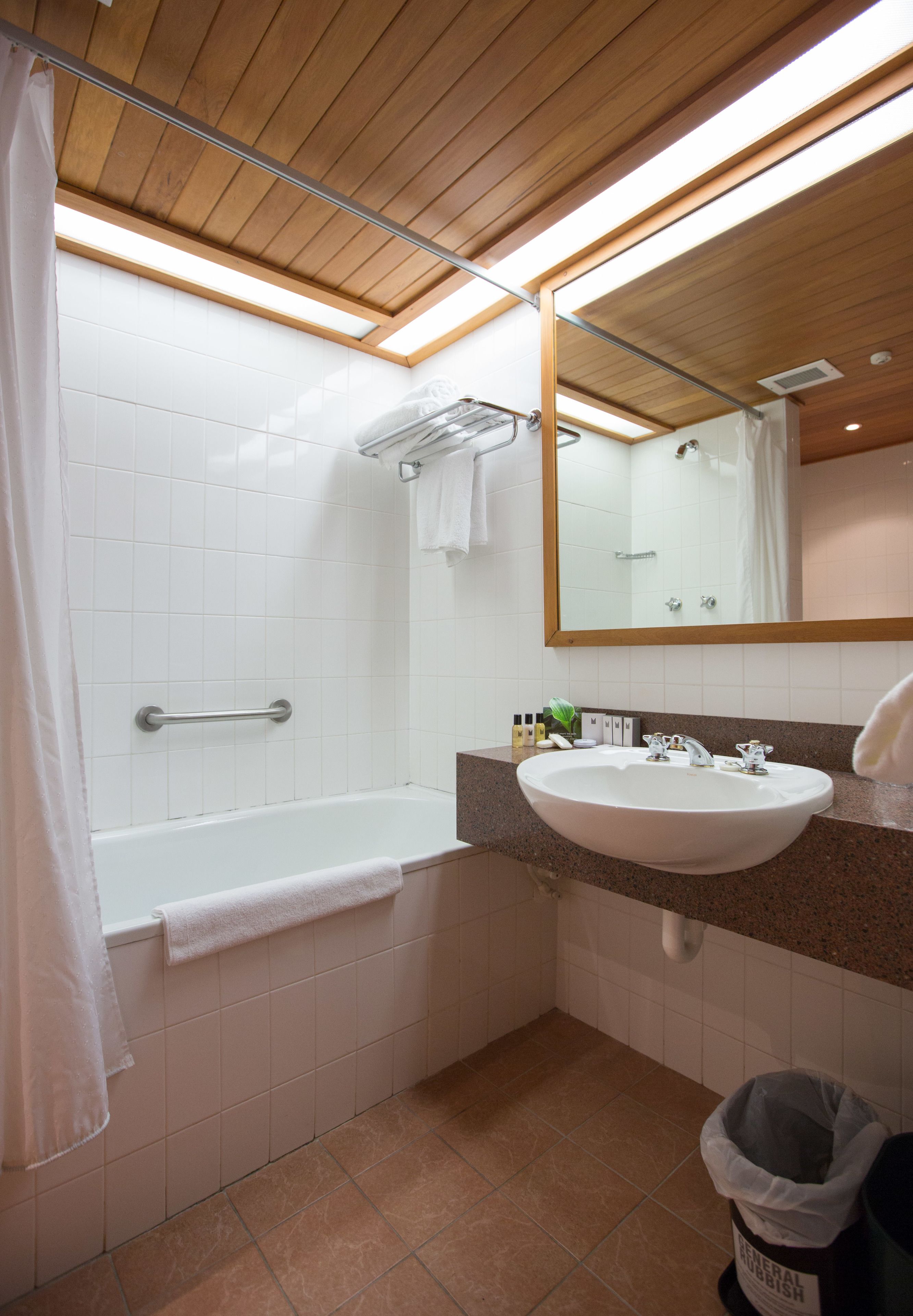 A bathroom with a bathtub, a sink, a mirror, and a trash bin.