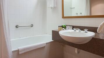 Un baño con bañera, lavamanos, espejo y cubo de basura.