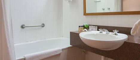Un baño con bañera, lavamanos, espejo y cubo de basura.