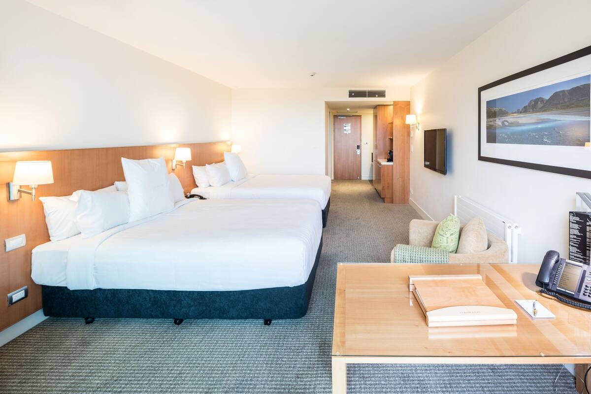 A hotel room with two beds, a desk with a telephone, a framed picture on the wall, and a carpeted floor.