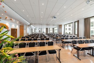 A conference room with rows of tables and chairs, large windows, and a ceiling with recessed lighting.
