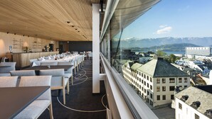 Un restaurant moderne avec un plafond haut, des lambris en bois et une vue sur le paysage urbain et les montagnes.