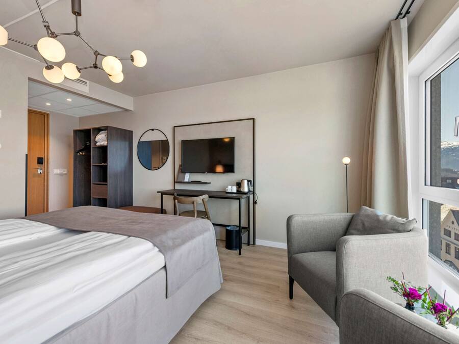 A hotel room with a bed, a desk, a chair, a TV, and a window with a view.