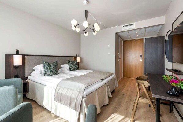 Una habitación de hotel moderna con una cama grande, lámparas de noche, un escritorio con silla y suelo de madera.