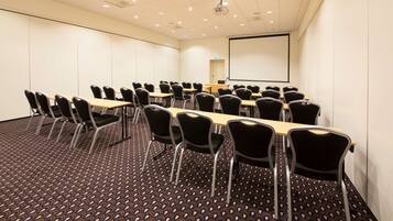 Une salle de conférence équipée d’un écran de projection, de plusieurs tables et de chaises.