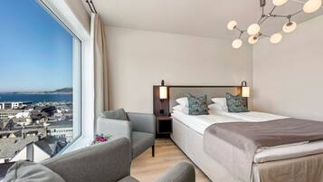 A hotel room with a large window, a bed, a sofa, and a nightstand.