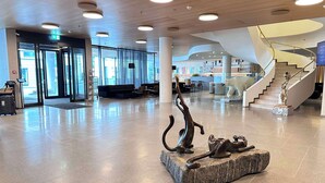 Un hall d’entrée spacieux au design moderne, agrémenté d’une sculpture centrale, d’un escalier et d’un espace d’accueil.