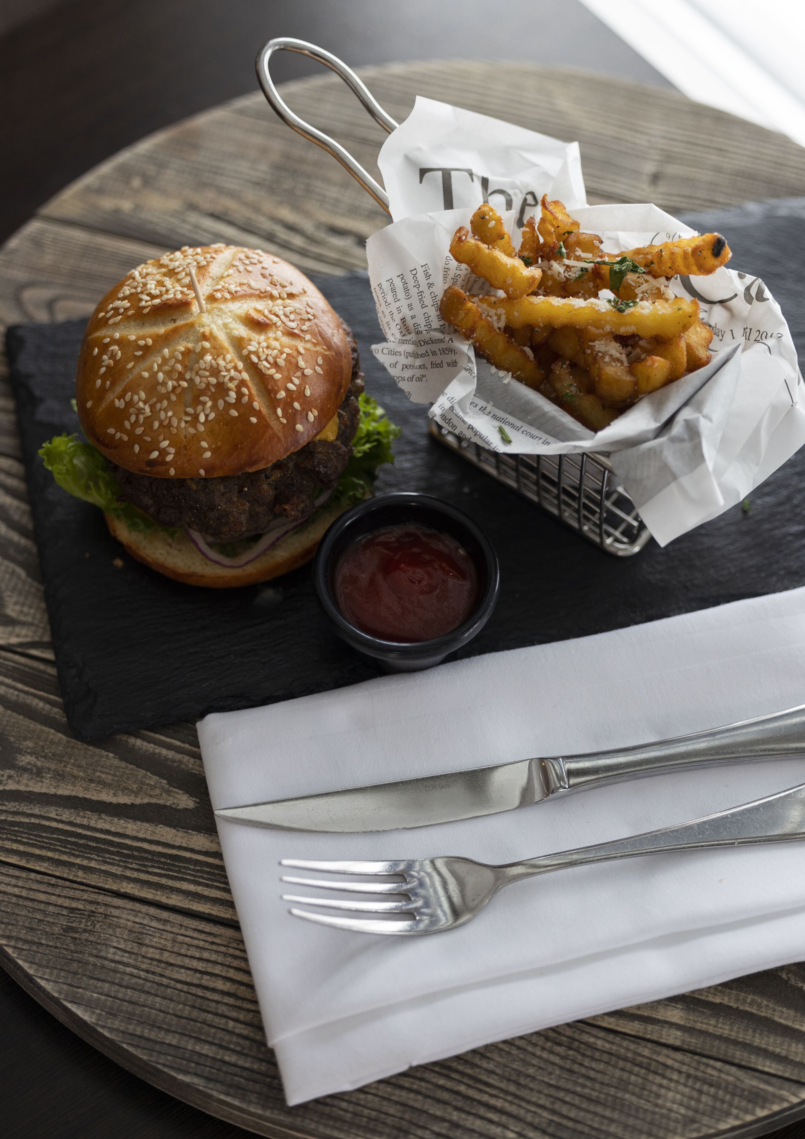 A burger with fries and ketchup on a slate plate.