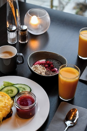 A breakfast setting with a plate of food, a bowl of cereal with berries, a glass of orange juice, and a candle on the table.