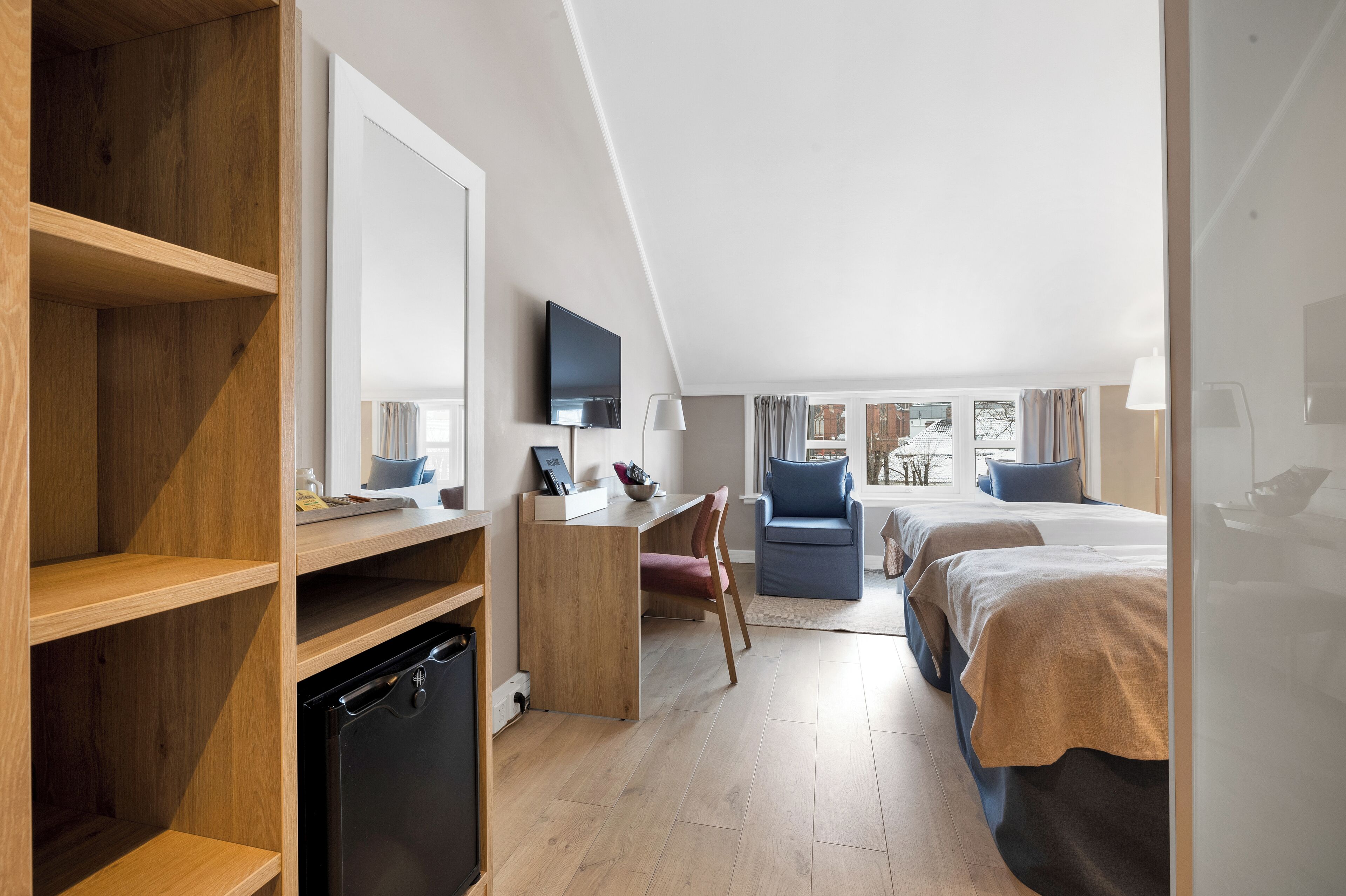 A modern hotel room with a wooden desk, a television, a bed, and a view of the outdoors.