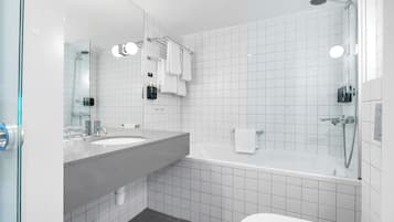 A modern bathroom with a large mirror, two sinks, a bathtub, and a toilet.