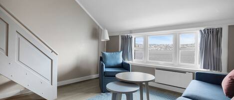 A modern living room with a sofa, a small table, and a view of the city through large windows.
