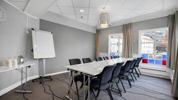 A conference room with a long table, chairs, a whiteboard, and a window with curtains.