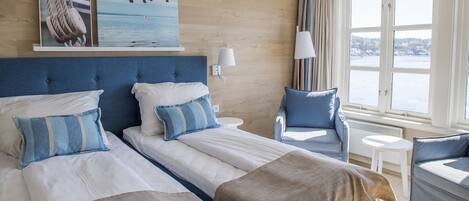 Hotelkamer met twee bedden, een stoel, een klein tafeltje en een raam met uitzicht op het water.