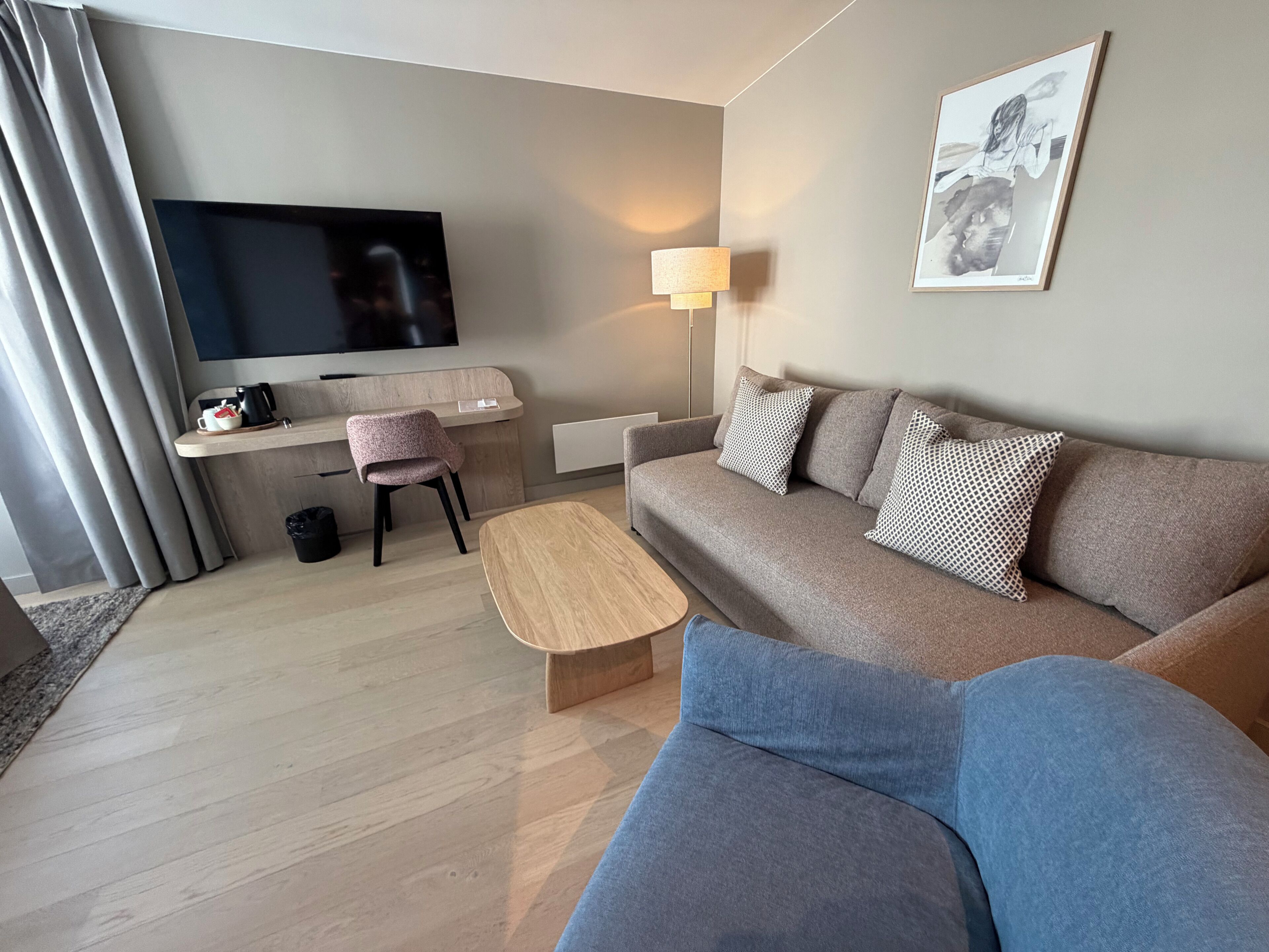 En moderne stue med et fladskærms-tv, en sofa, et sofabord, et skrivebord med en stol og en lampe.