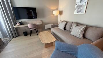 En moderne stue med et fladskærms-tv, en sofa, et sofabord, et skrivebord med en stol og en lampe.