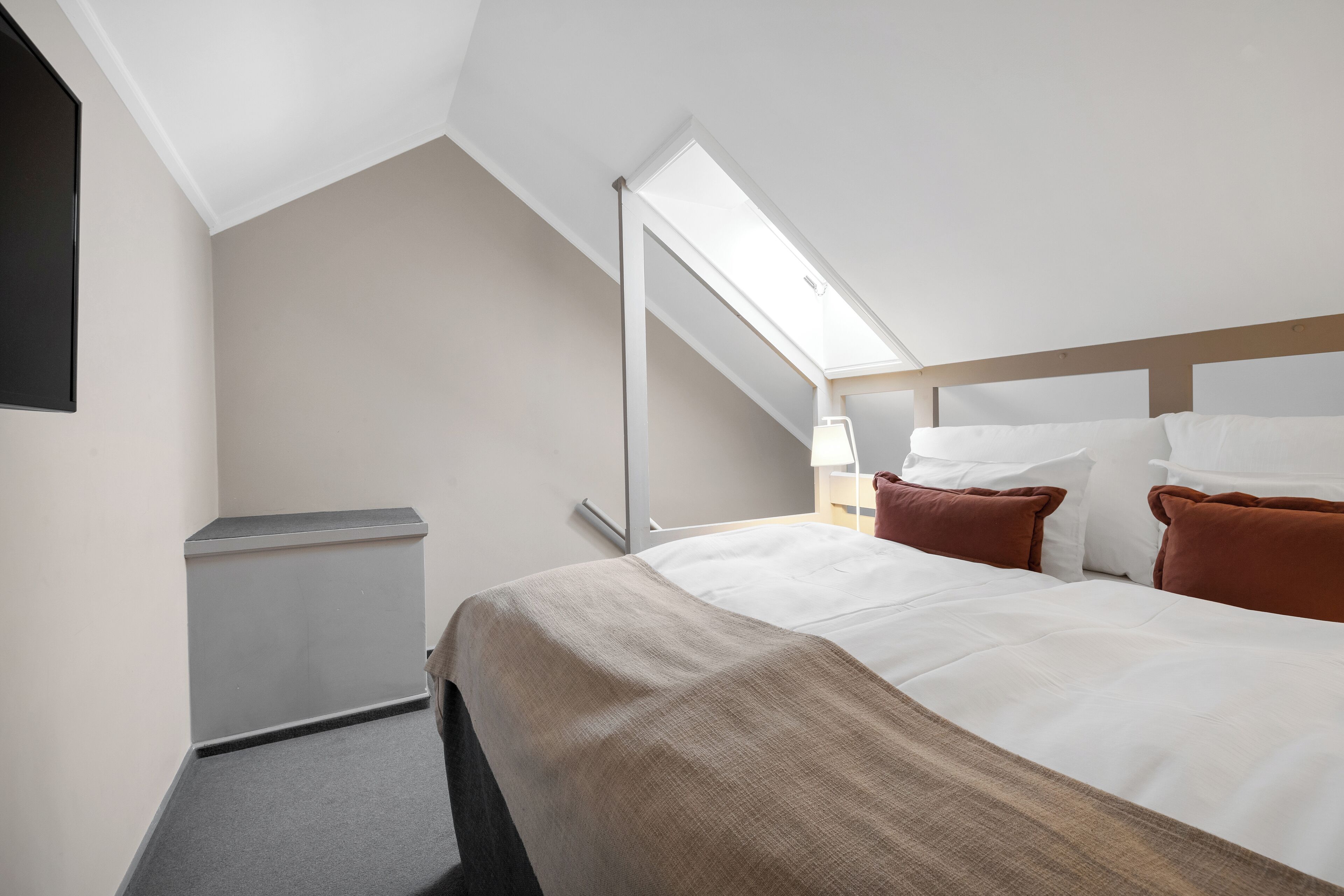 A hotel room with a bed, a desk, a chair, a window, and a ceiling light.