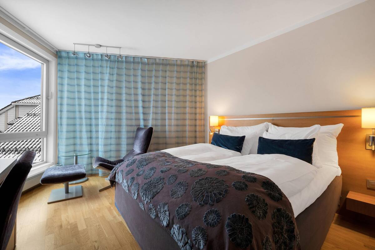 Een hotelkamer met een bed, een stoel, een bureau en een raam met gordijnen.