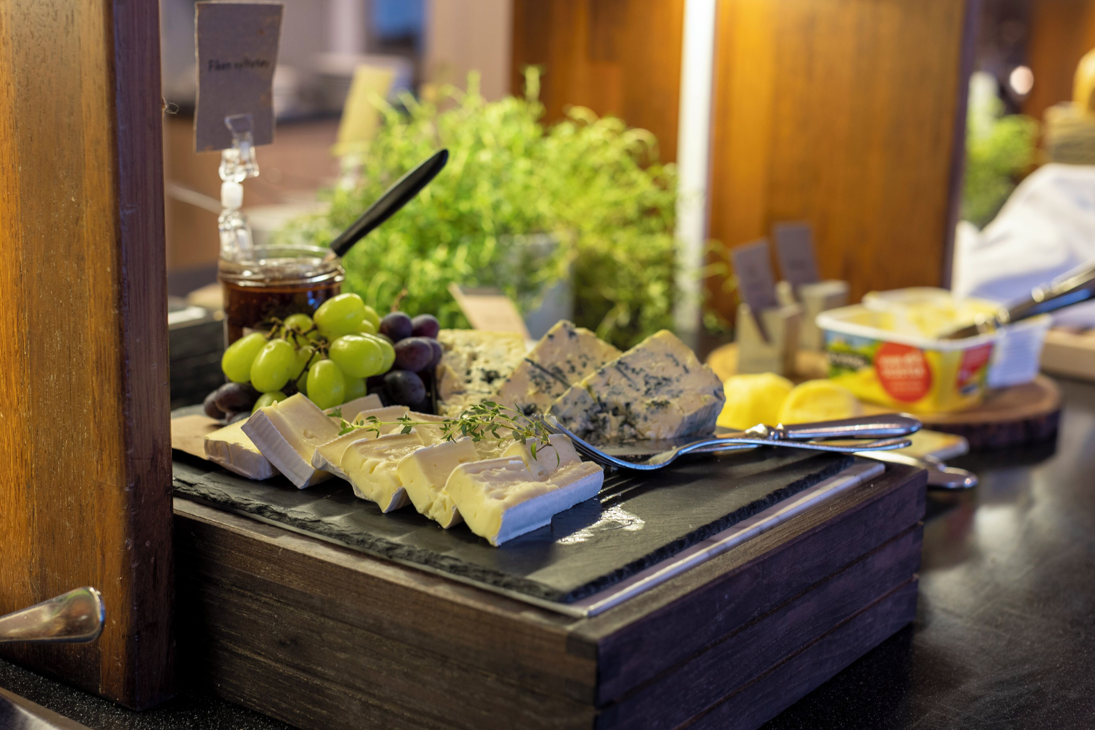 A cheese board with various cheeses, grapes, and a honey dipper.