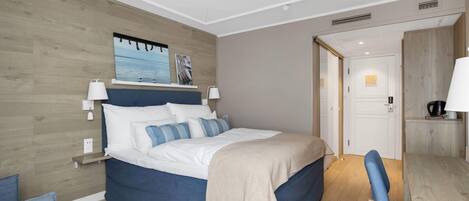Una habitación de hotel moderna con una cama grande, lámparas de noche, un cabecero de madera, un escritorio pequeño y vista al mar a través de una ventana.