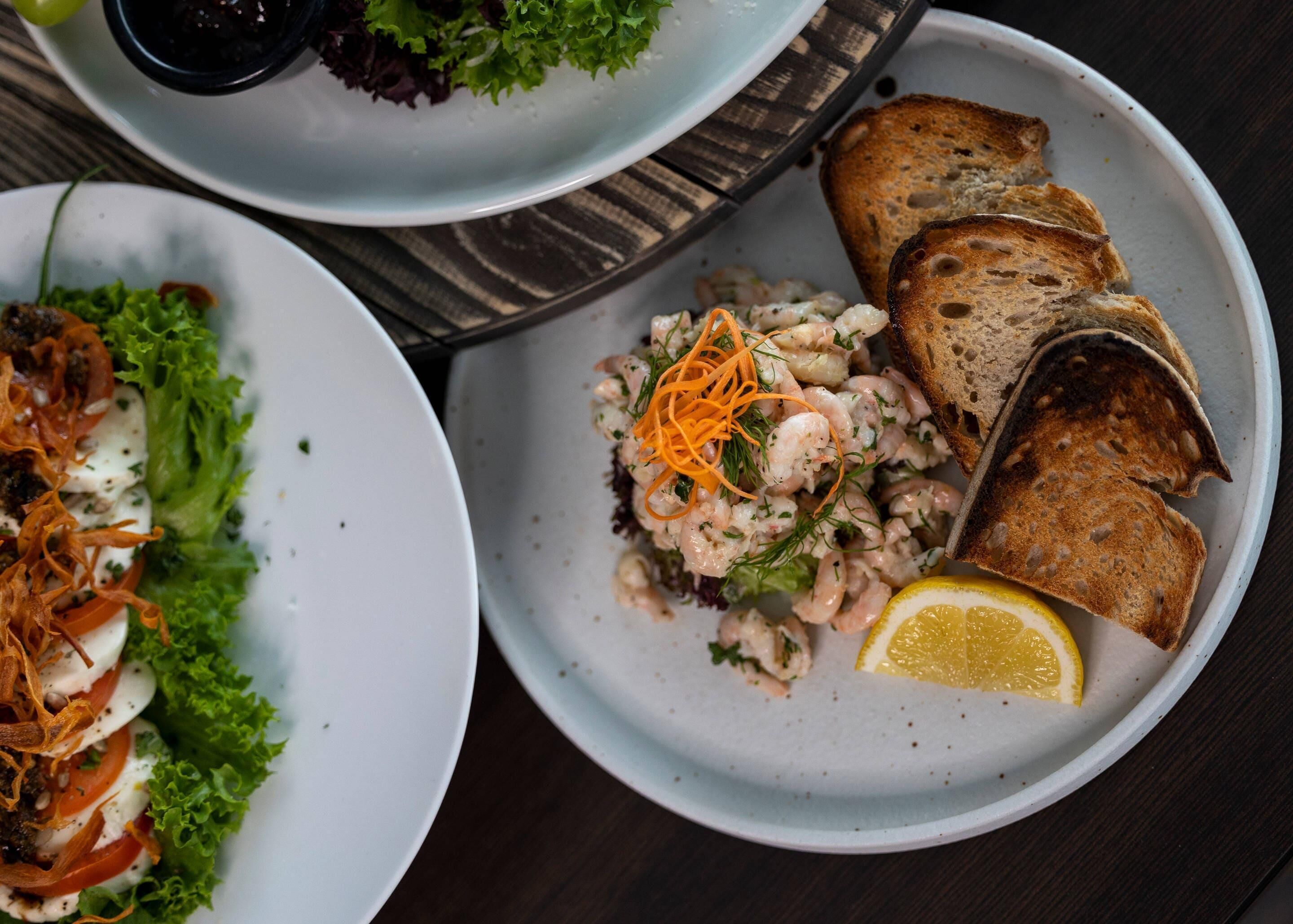 A table with plates of food, including a salad, shrimp, and bread.