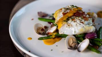 A white plate with a poached egg, green beans, clams, and a drizzle of sauce.