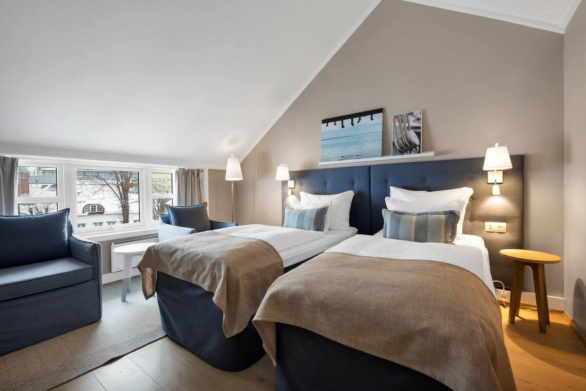 Een hotelkamer met twee bedden, een bank, een tafeltje en uitzicht op buiten.