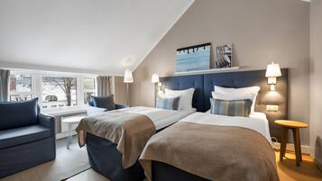 A hotel room with two beds, a sofa, a small table, and a view of the outside.