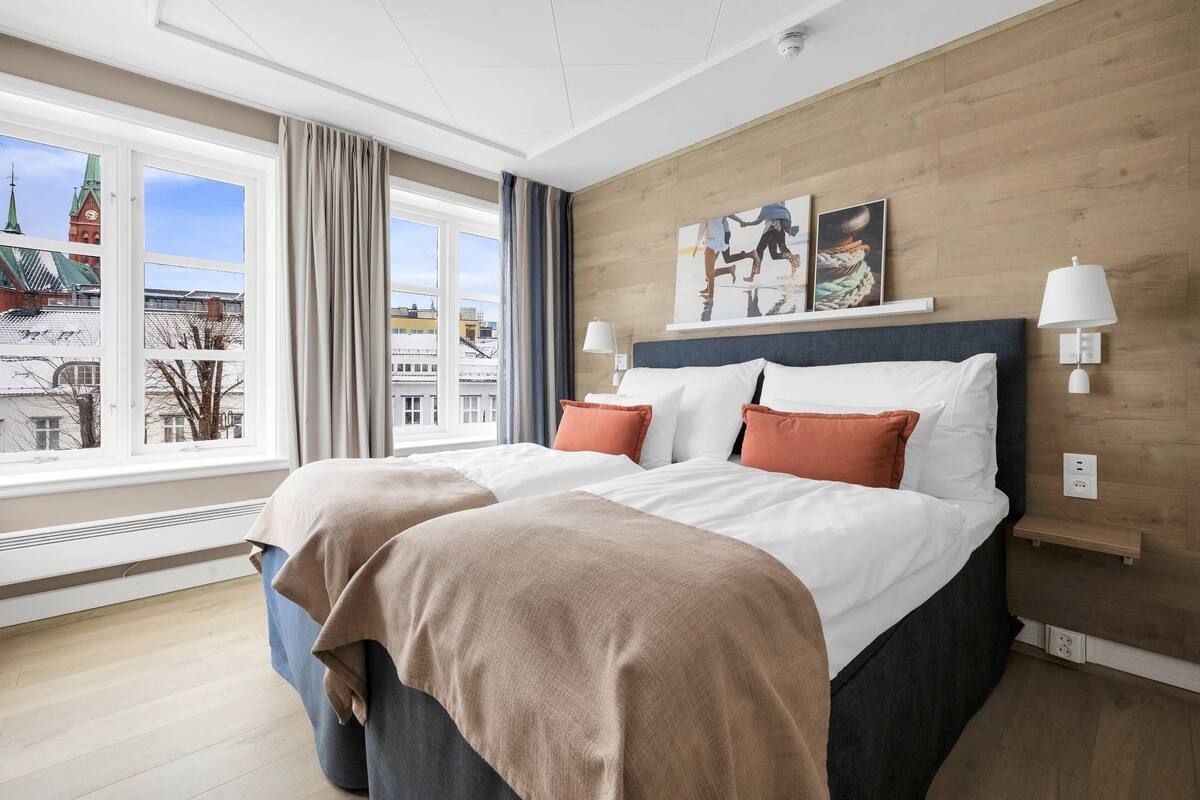 Een hotelkamer met een groot bed, uitzicht op een stadslandschap, een houten wand en een schilderij.