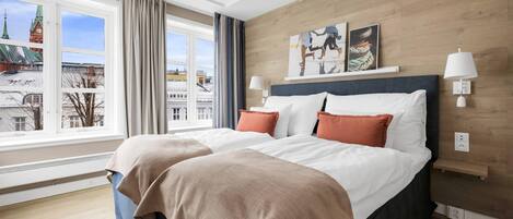 A hotel room with a large bed, a view of a cityscape, a wooden wall, and a painting.