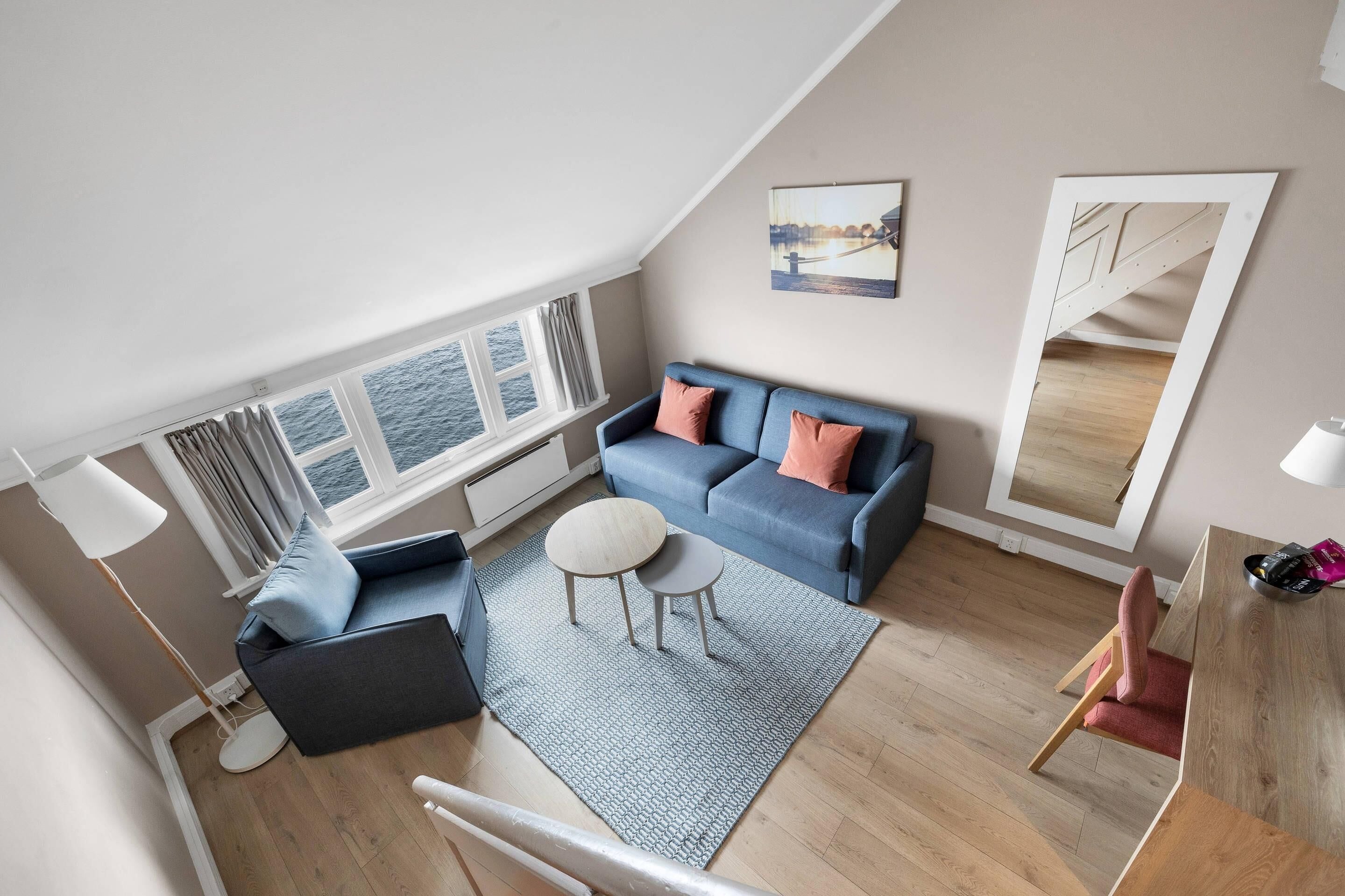 En moderne stue med en blå sofa, et rundt sofabord og havudsigt gennem store vinduer.