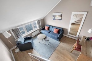 Ein modernes Wohnzimmer mit einem blauen Sofa, einem runden Couchtisch und Meerblick durch große Fenster.