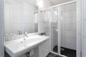 Une salle de bain moderne avec un lavabo blanc, un miroir et une cabine de douche en verre.