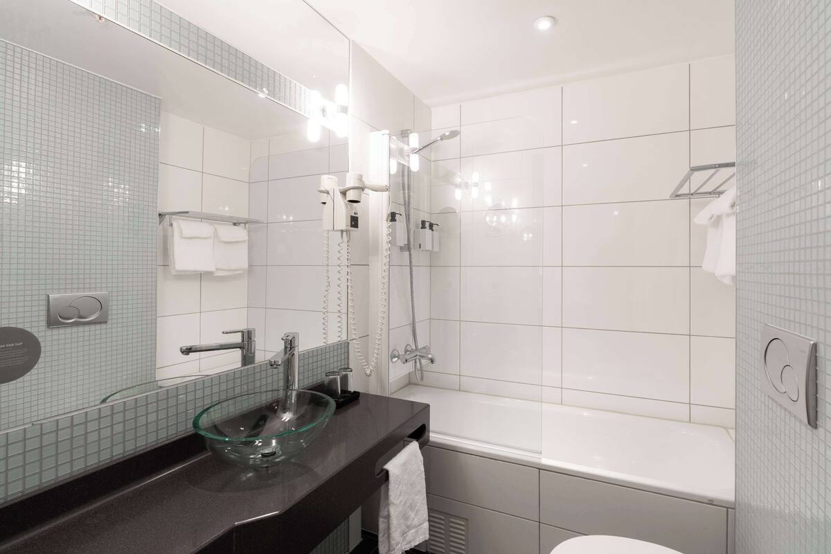 A modern bathroom with a glass bowl sink, a large mirror, a bathtub, and a shower.