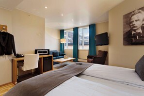 Une chambre d’hôtel avec un lit, un bureau avec un ordinateur portable, une chaise, une télévision et une fenêtre avec des rideaux.