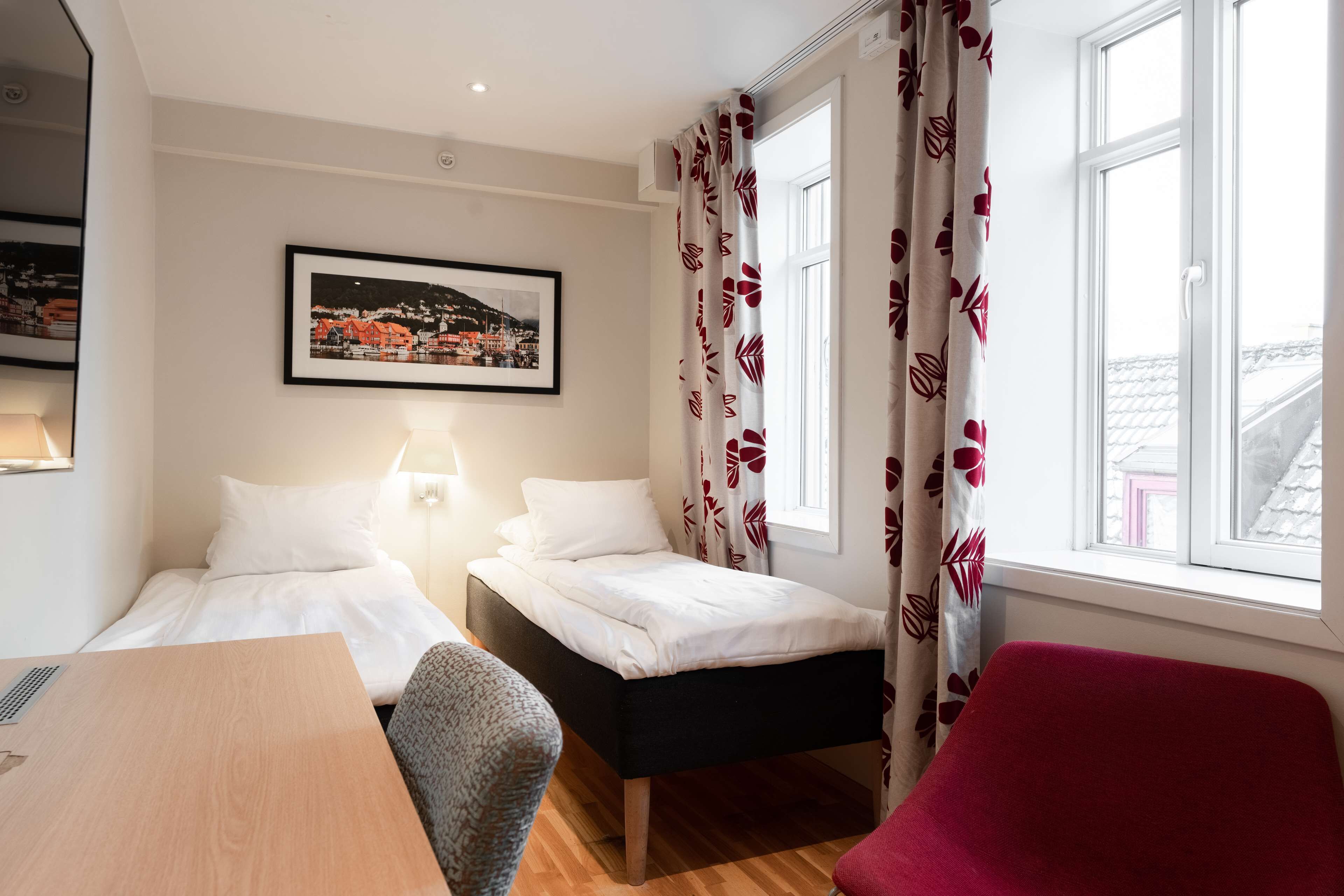 A hotel room with two single beds, a desk, a chair, and a window with curtains.