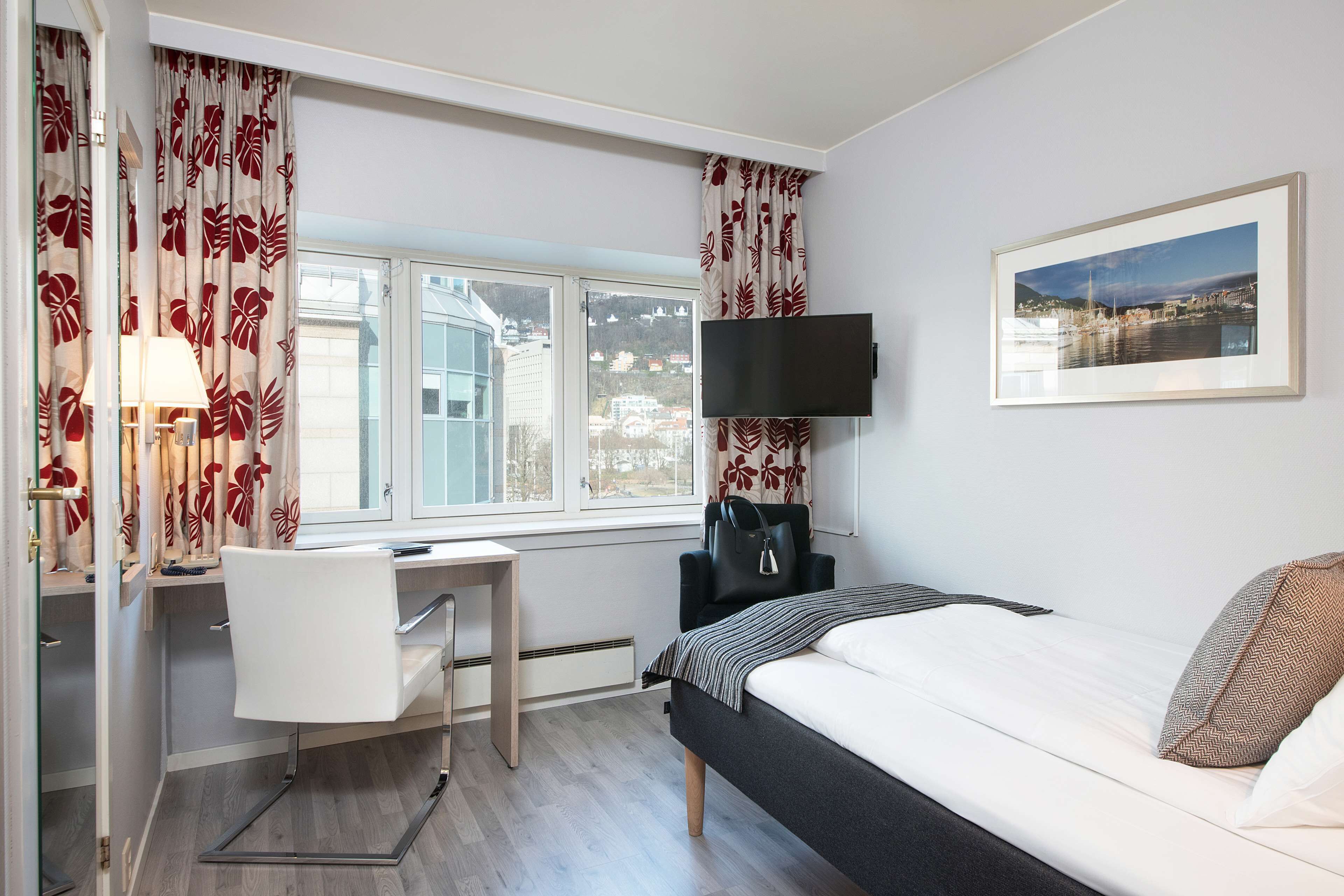 Habitación de hotel con cama, escritorio, silla y televisión instalada en la pared.