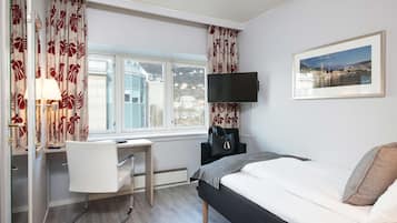 Habitación de hotel con cama, escritorio, silla y televisión instalada en la pared.