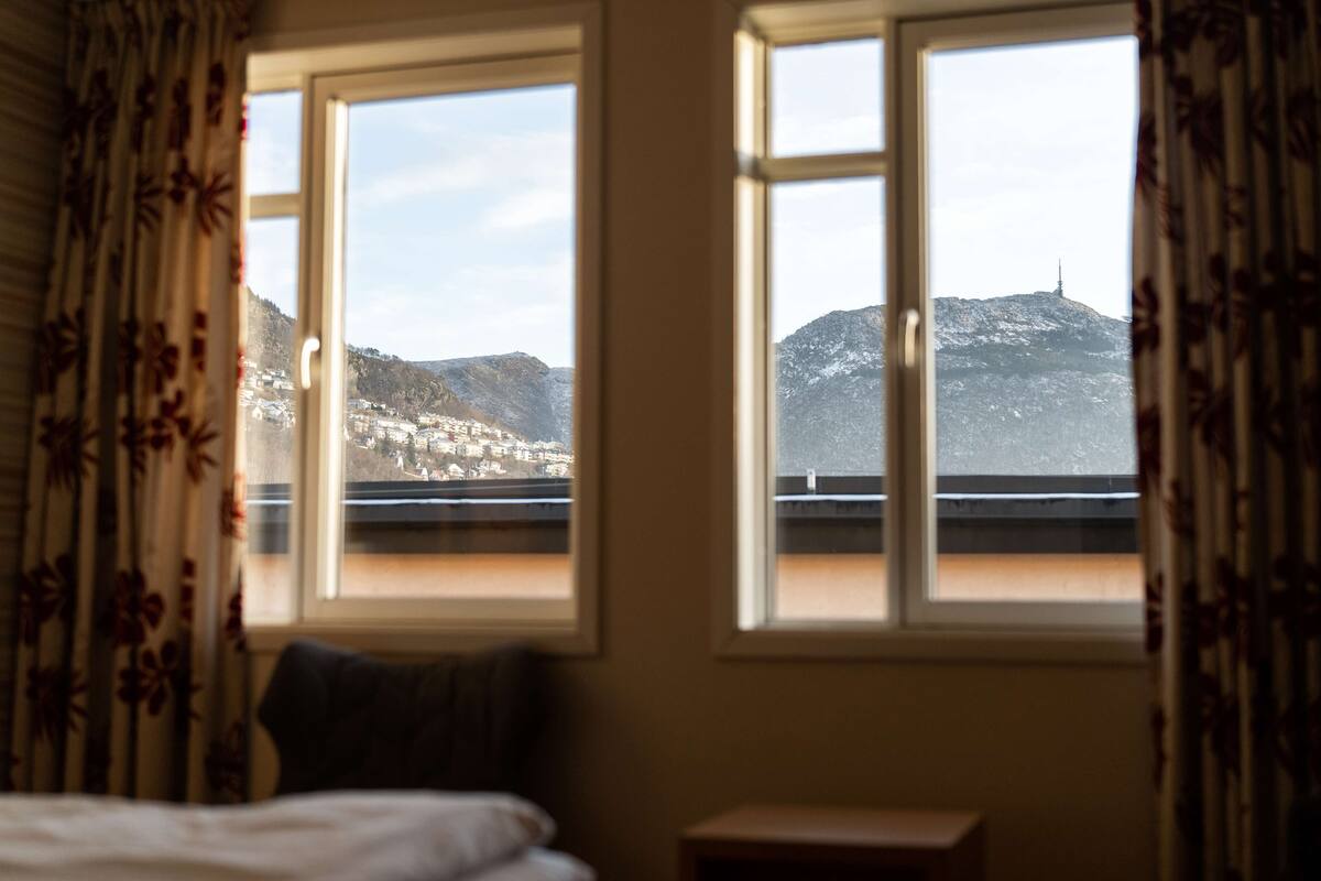 A hotel room with two windows offering a view of a mountainous landscape and a distant tower.