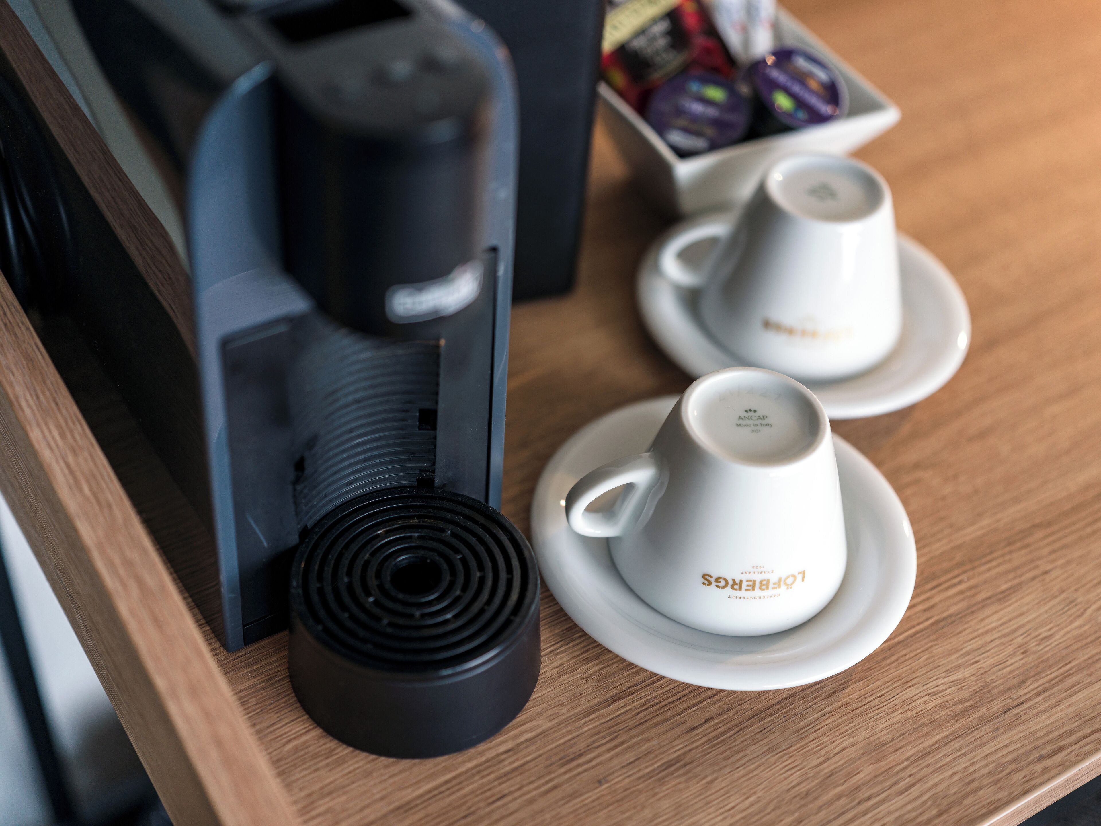Une machine à café avec deux tasses blanches posées sur des soucoupes, le tout sur une table en bois. Les soucoupes sont marquées du mot « Lobres ».
