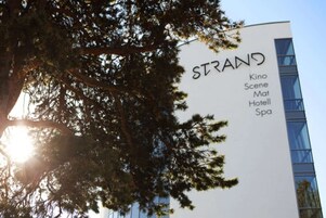 Un edificio con un letrero que dice "STRAND" y enumera comodidades como Kine, Scene, Mat, Hotel y Spa.
